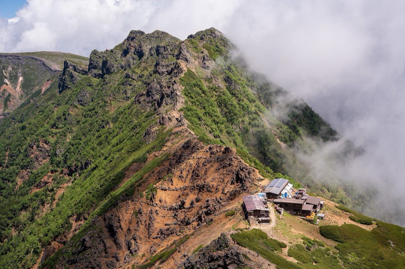 雲が流れる稜線と、尾根の上に建つ山小屋(八ヶ岳)